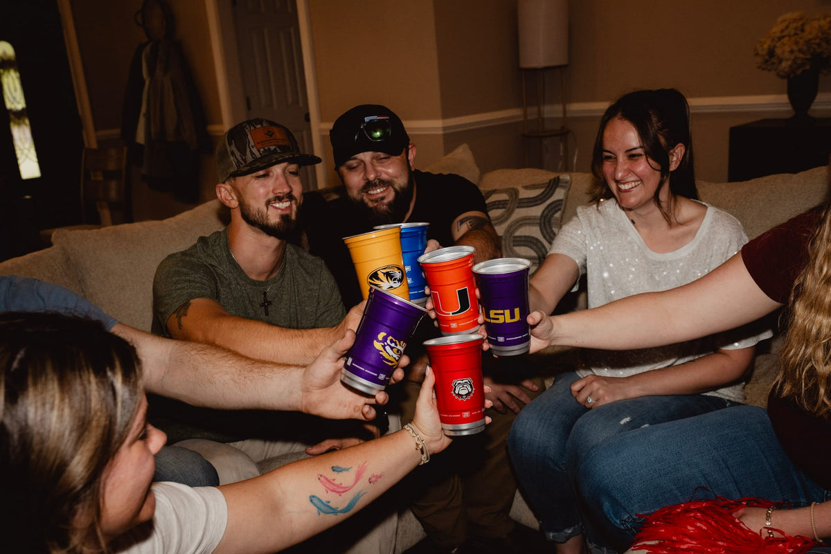 Friends toasting officially licensed college Top Cup aluminum cups at a game day watch party